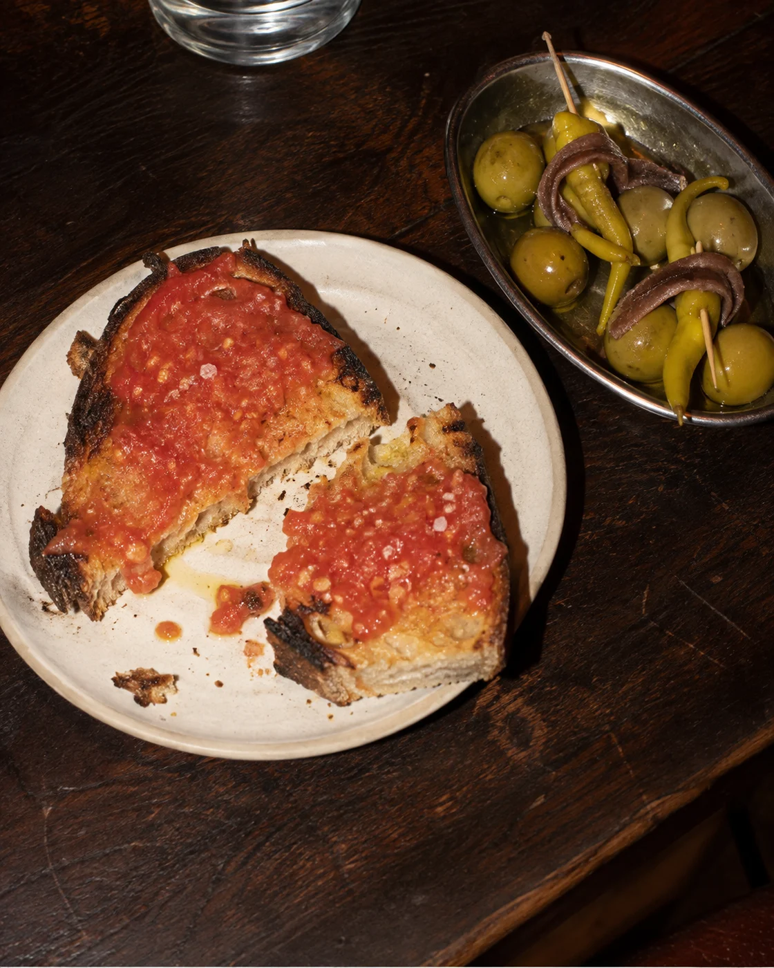 Tomato toast, olives and anchovy skewers on a well-used wooden bar counter