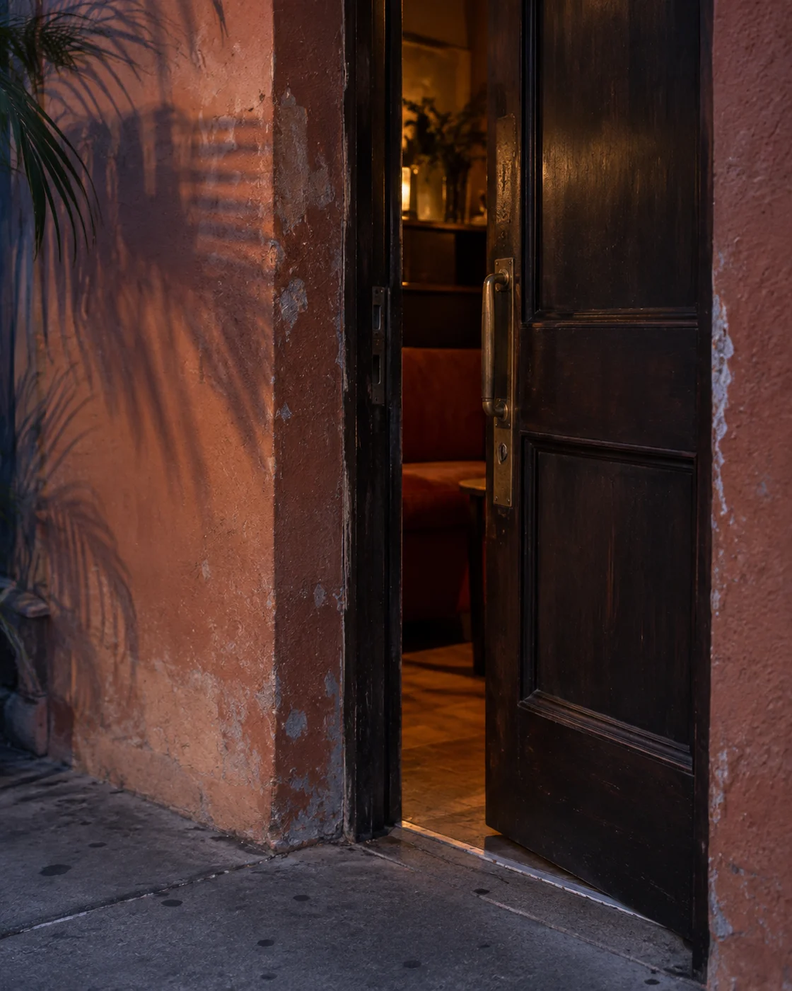 Warm light through an open wooden doorway at dusk, beside a weathered terracotta wall